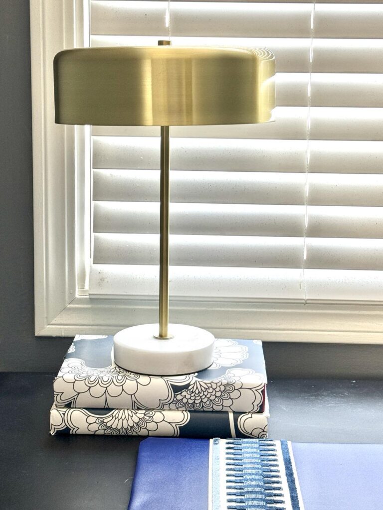 how to decorate a desk in a bedroom by using a gold lamp sitting on top of a stack of books.