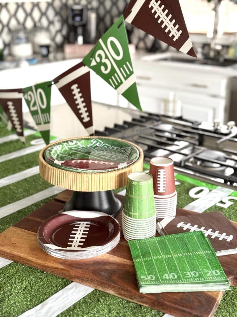 Football-themed plates and napkins on a wood cutting board on top of a Super Bowl table.