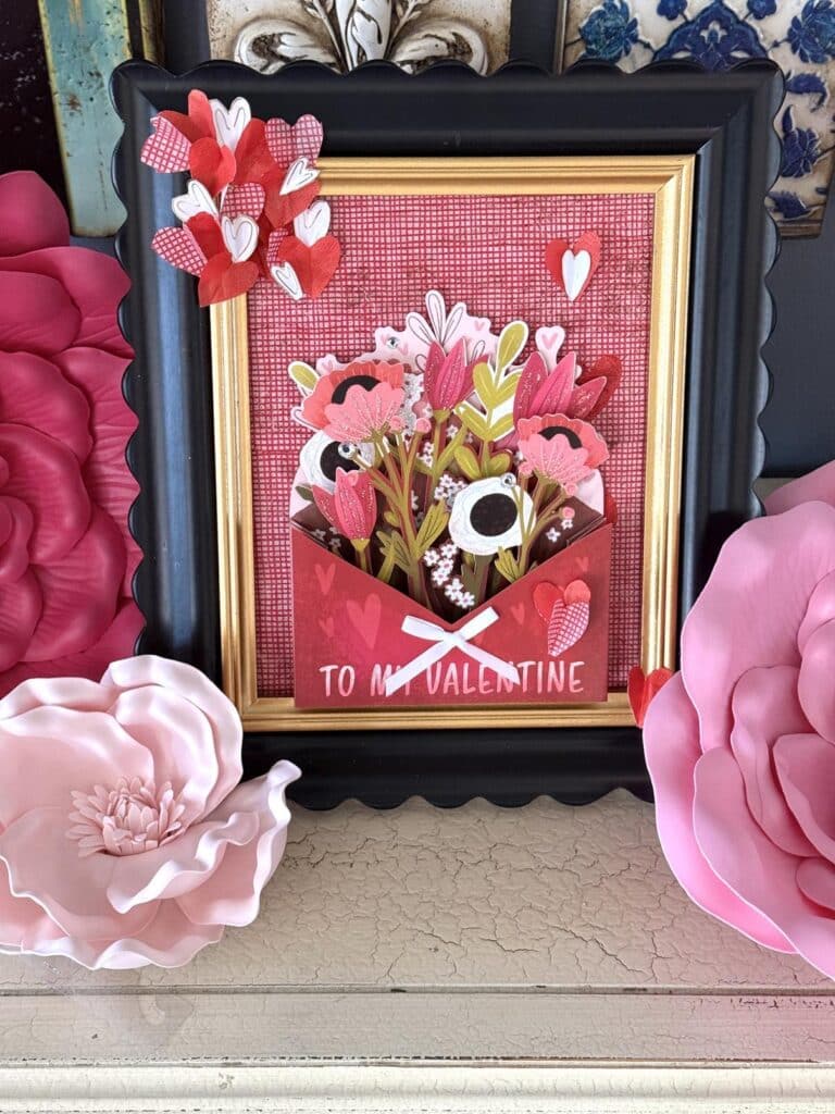 DIY frame Valentine art nestled among pink and red faux flowers.