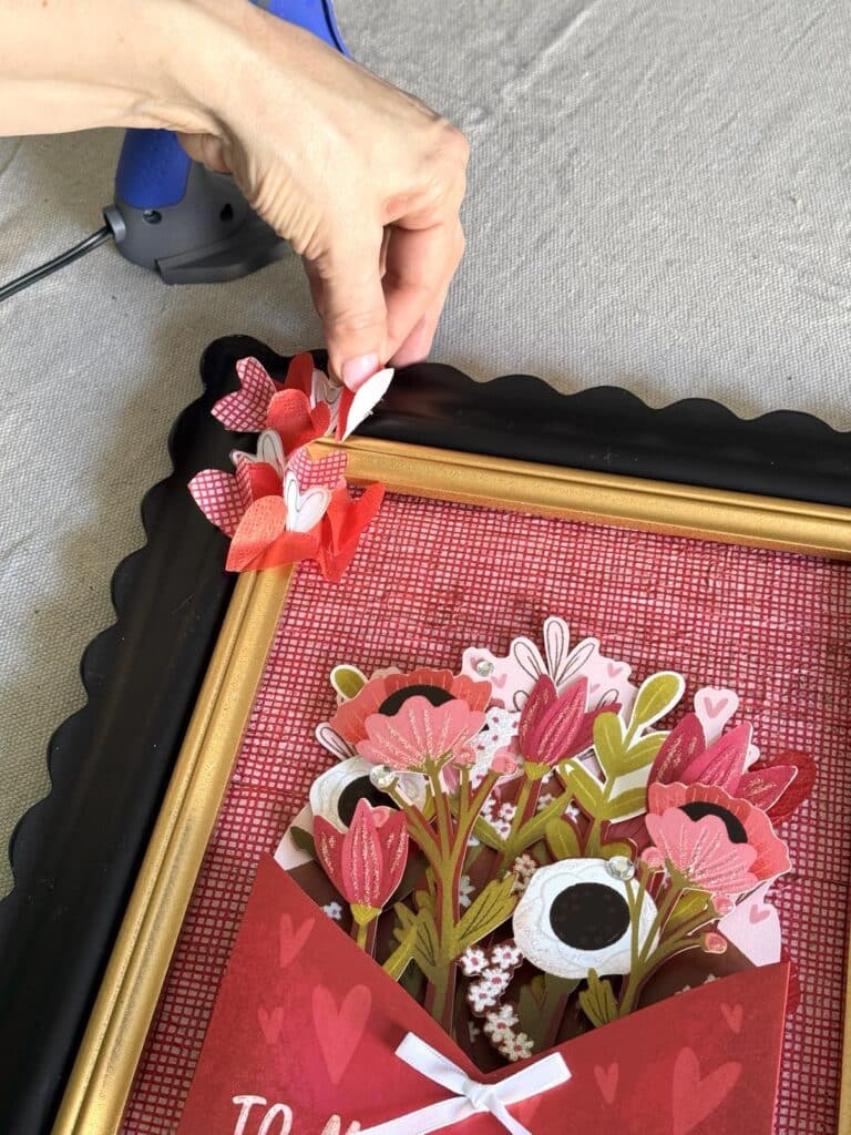 Gluing fold paper hearts onto a photo frame as 3D Valentine art.