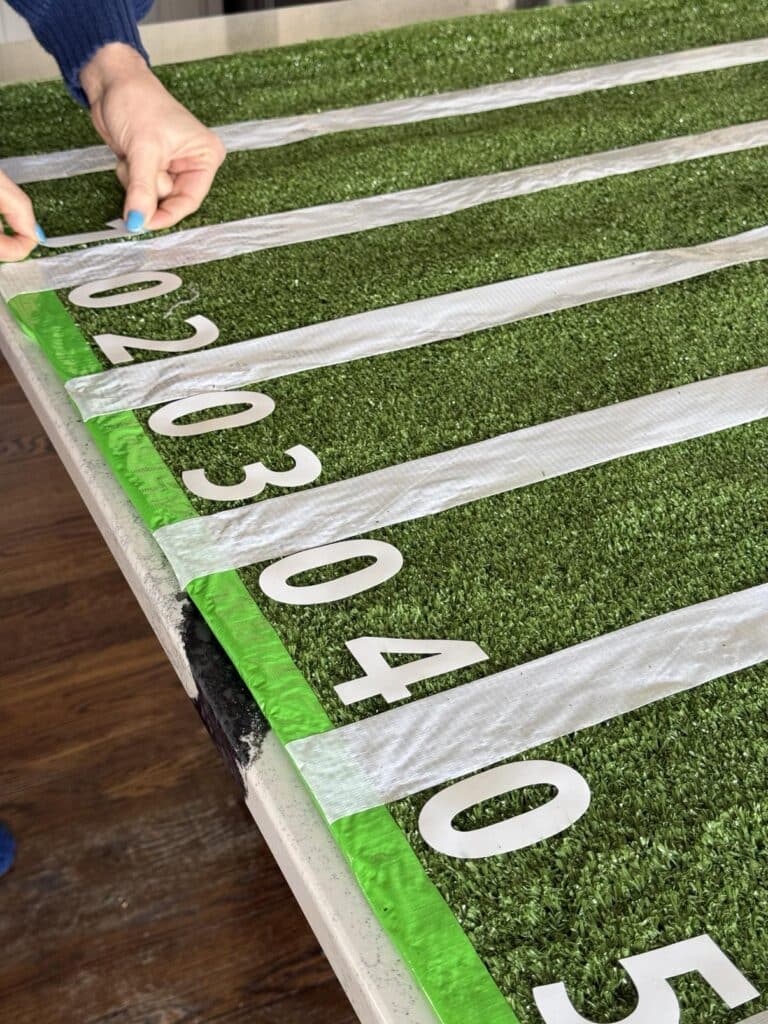 Pressing number stickers on either side of duct tape yard lines on Super Bowl table.