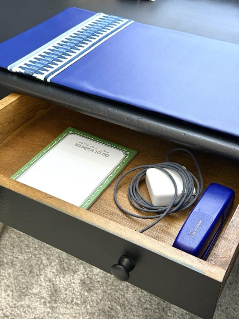 A bedroom desk drawer pulled out to reveal a notepad, laptop charger, and stapler.