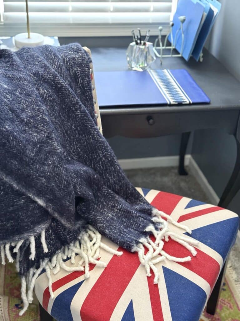 A blue throw blanket draped over a desk chair is a stylish way for how to decorate a desk in a bedroom.