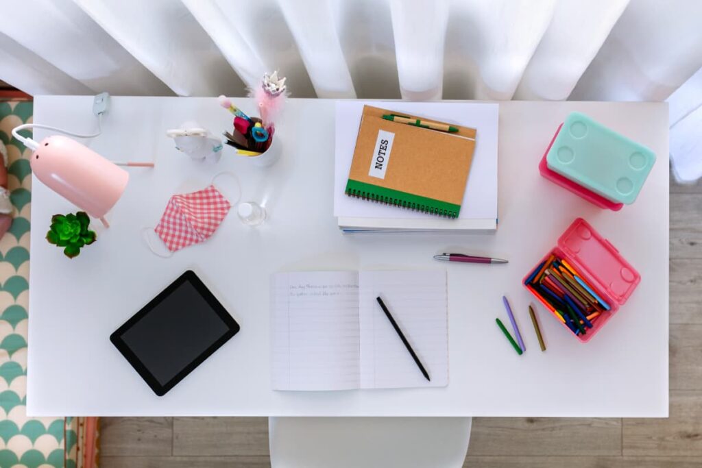 The top of a desk with notepads, pens, pencils, ipad, and desk lamp.