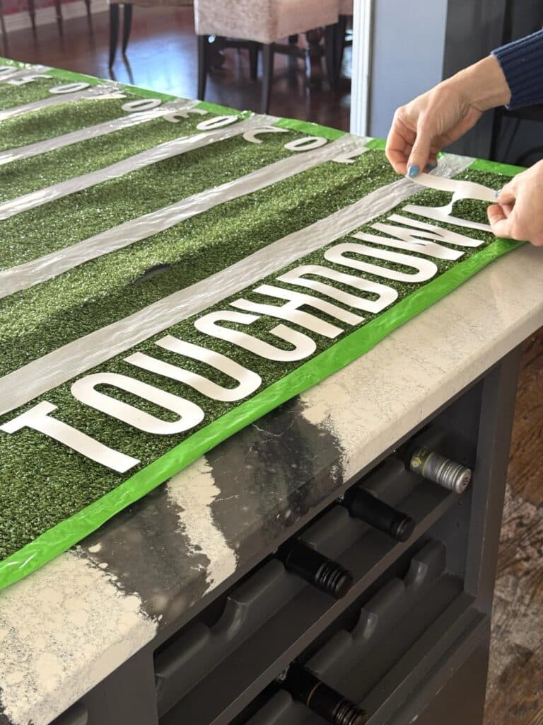 Pressing letter stickers onto fake grass to spell out the word "Touchdown."