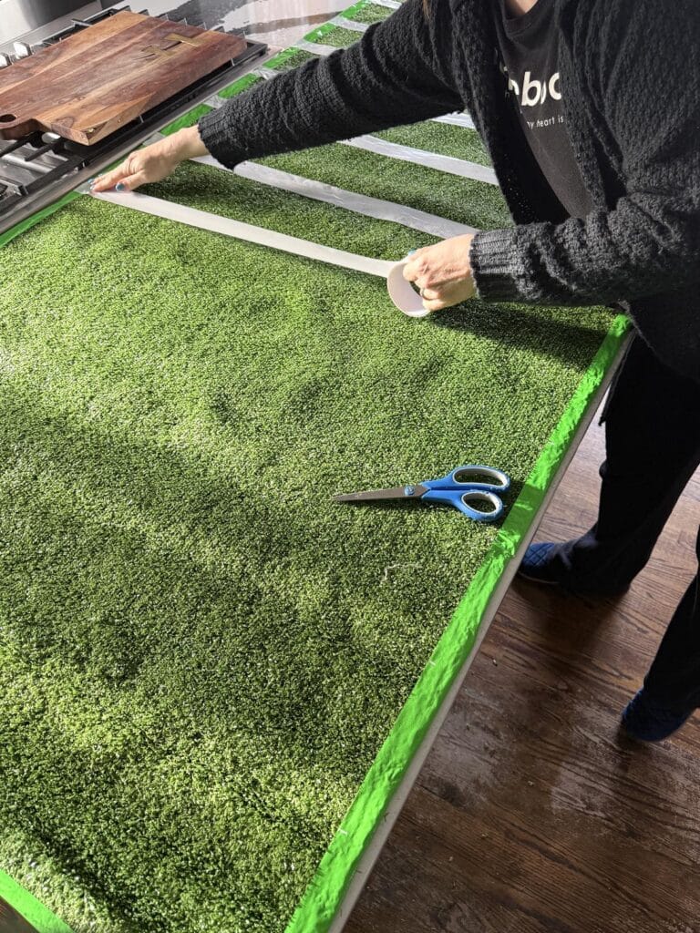 Applying white duct tape to artificial grass to create a football field Super Bowl table.