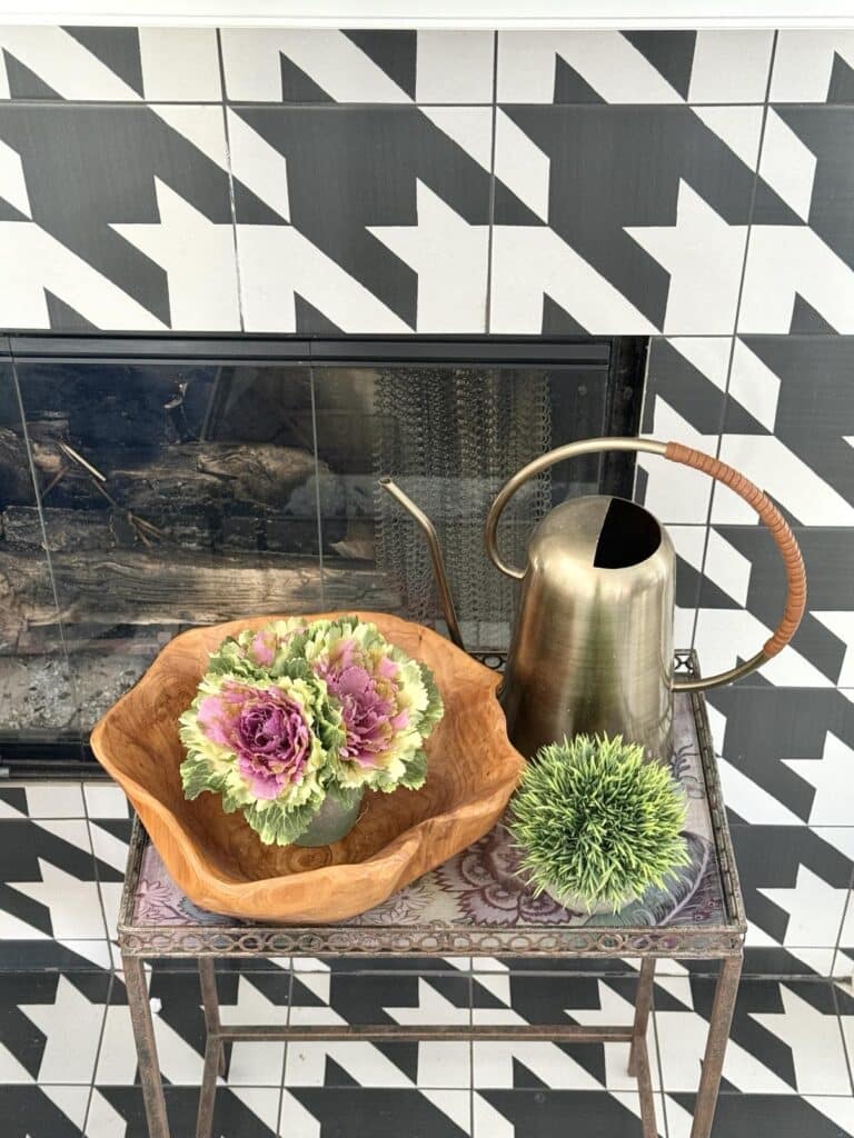 A small table sitting in front of a fireplace holding a wood bowl and faux spring plants.