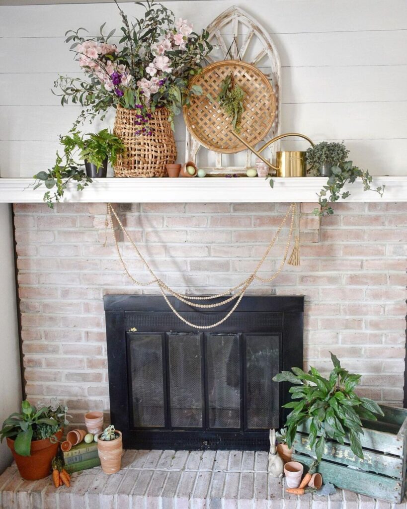 A brick fireplace styled for spring with basket, bead garland, green plants, and a wood window frame.