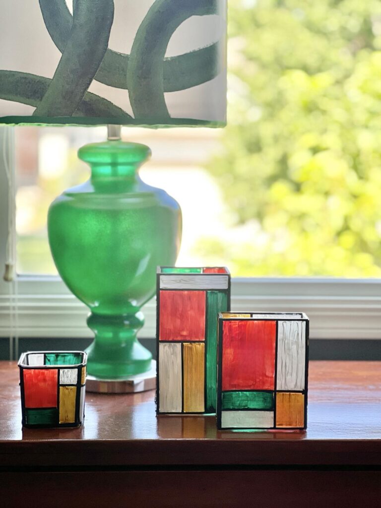 paint a glass vase - three painted vases beside a green lamp on a table.