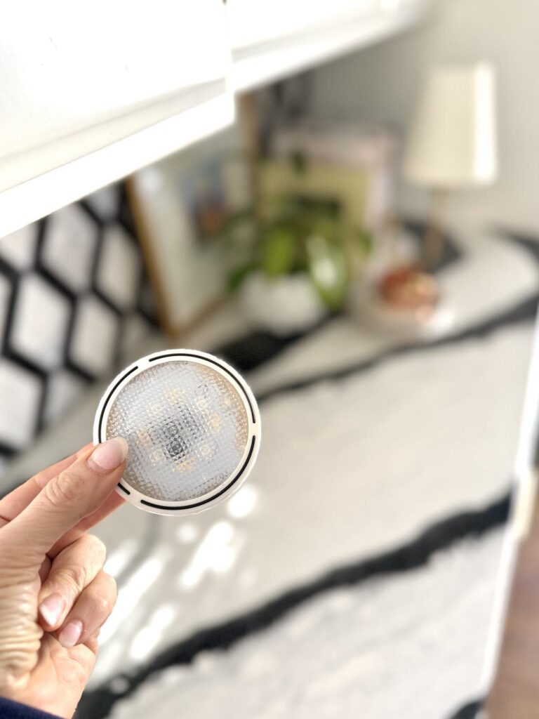 A woman's hand holding a white under-cabinet puck light.