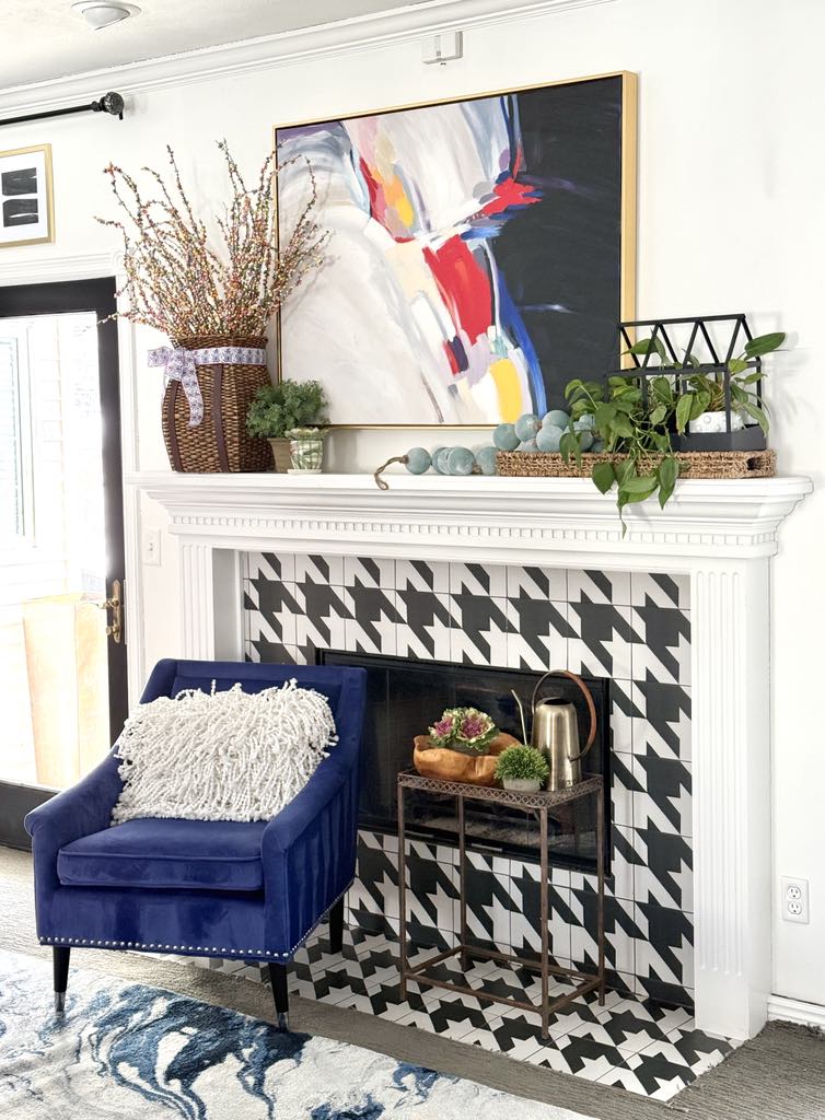 A fireplace mantel decorated for spring with home decor, greenery, and artwork.