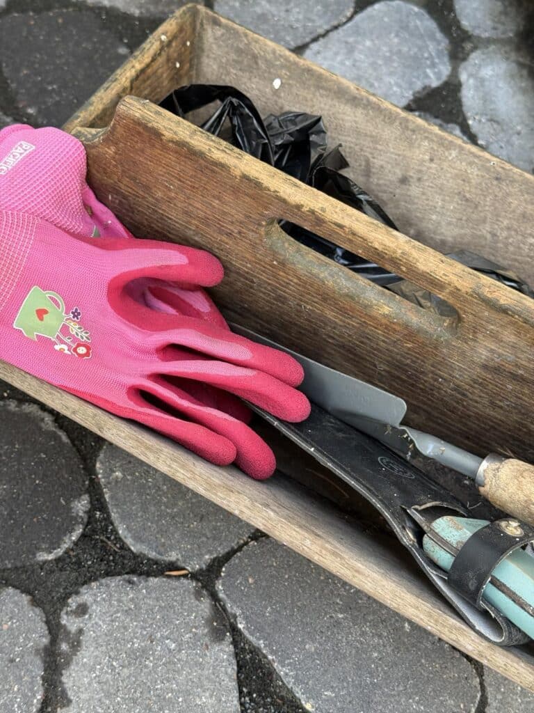 A wood garden tote holding garden tools and gloves.