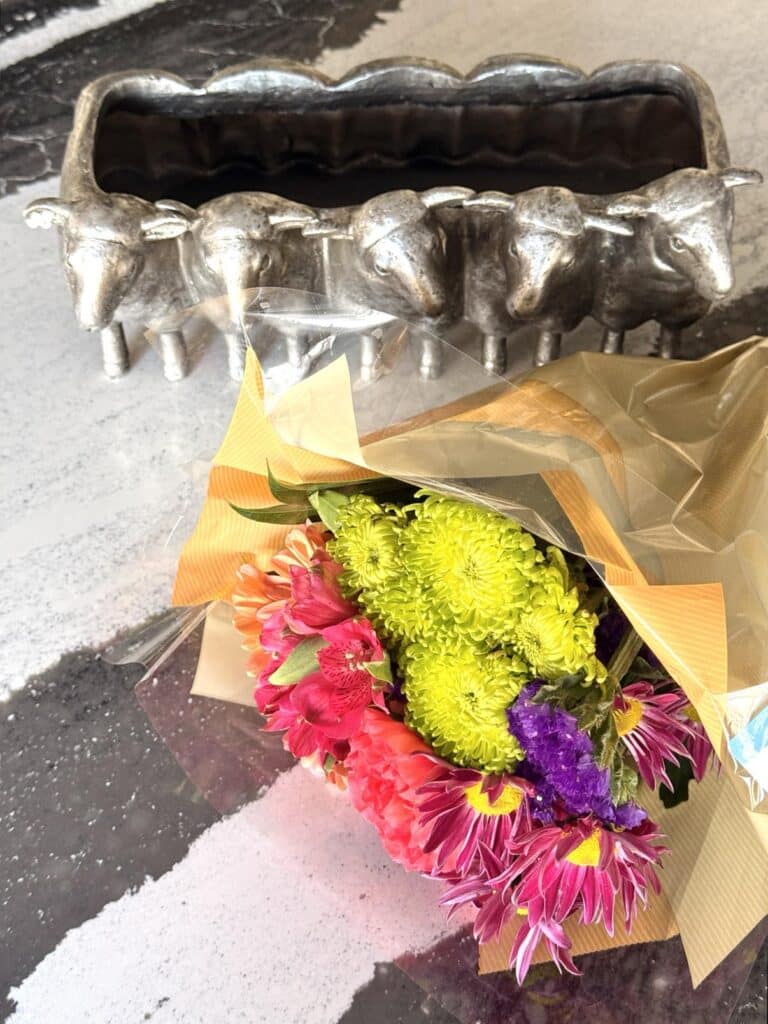 A bouquet of grocery store flowers and a floral container featuring 5 lambs.