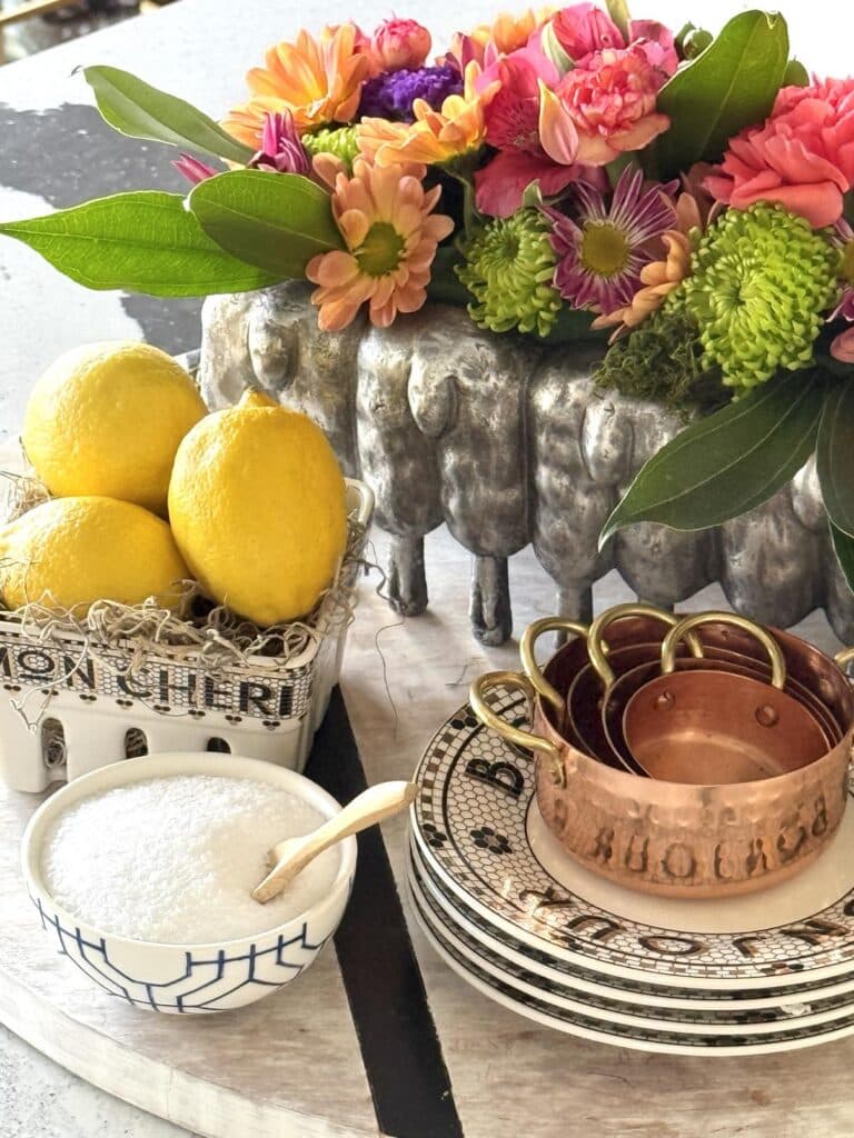 A bowl of lemons, copper measuring cups, and a salt cellar.