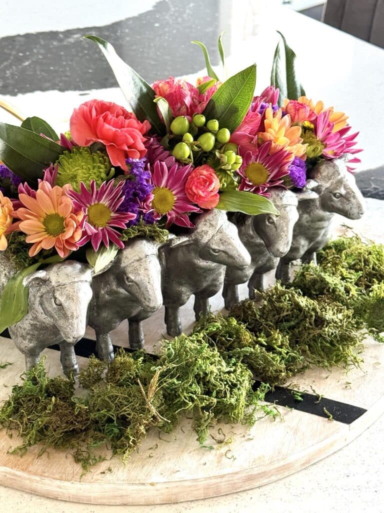 A spring floral centerpiece featuring bright flowers and a sheep themed planter.