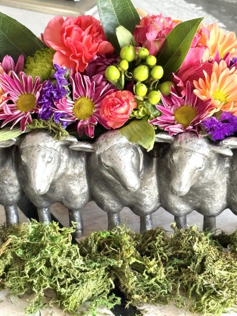 Brightly colored flowers in a sheep themed planter with green moss laid in front.